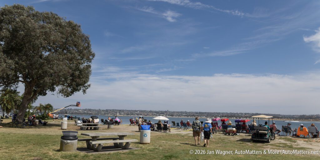 People sitting in folding chairs along a waterfront park, with a golf cart parked in the foreground.