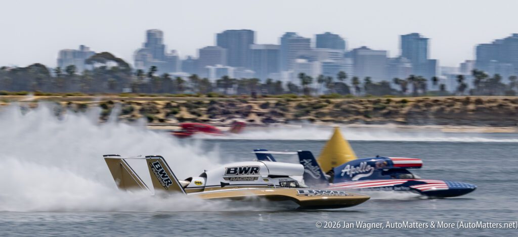 Two hydroplane racing boats speed across the water in front of a city skyline.