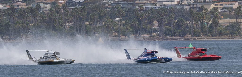 Three unlimited hydroplane race boats speeding across the water, kicking up large wakes.