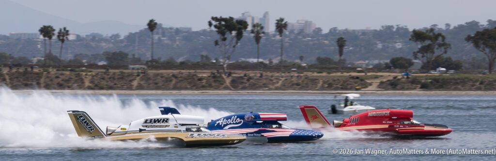 Three hydroplane race boats speeding across a body of water, leaving trails of spray.