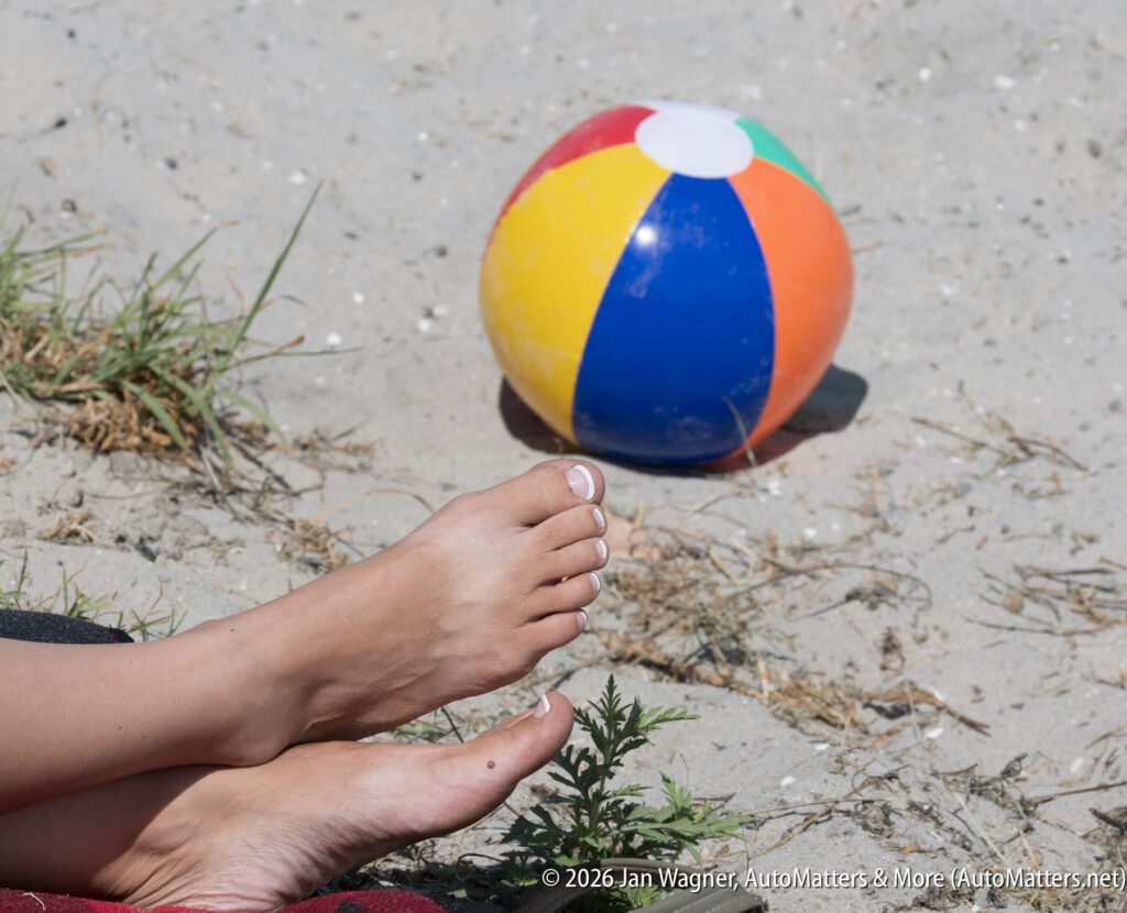 A person’s feet resting on sandy ground near a multicolored beach ball.
