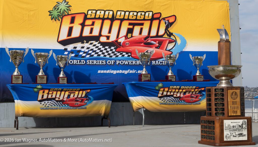 Seven trophies displayed on tables in front of a San Diego Bayfair banner, with the large Bill Muncey Cup trophy in the foreground.