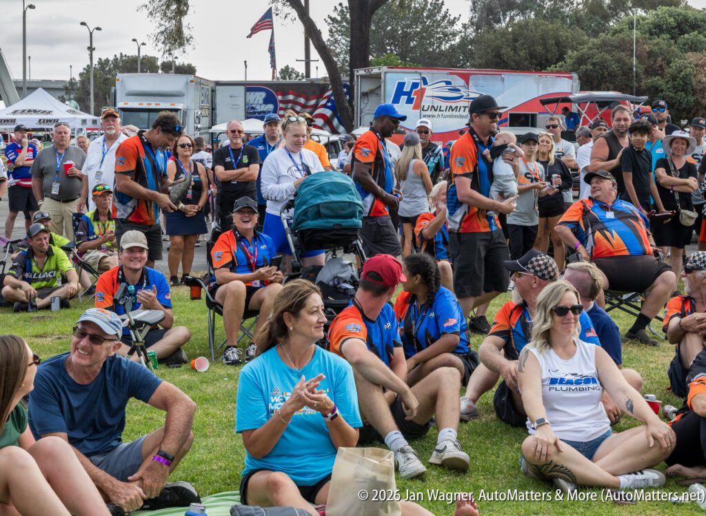 A large crowd of people sitting and standing on a lawn at an outdoor event, many wearing matching orange, blue, and black uniforms.