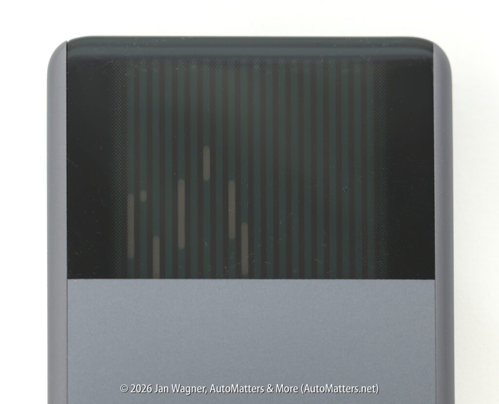 Close-up of the top portion of a gray and black electronic device, showing a patterned black section above a solid gray area. Text copyright is visible at the bottom.