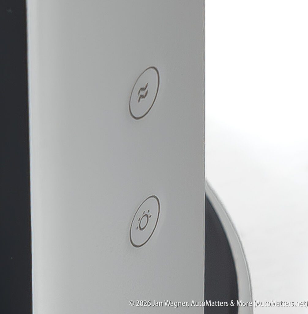Close-up of two circular buttons on a white electronic device, one with a wavy line symbol and one with a sun icon. Part of a black screen is visible on the left side.