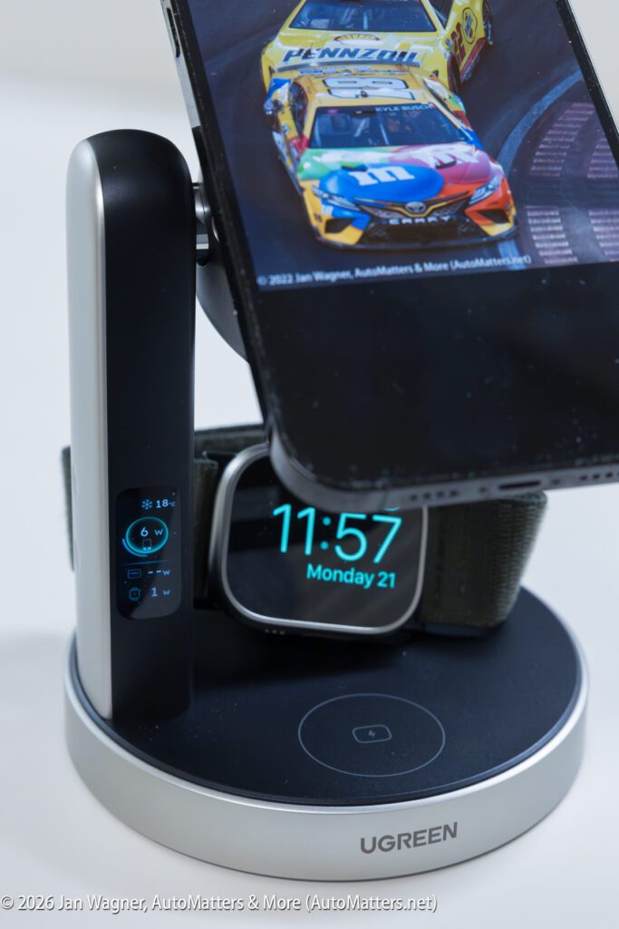 A smartphone, smartwatch, and tablet are docked on a UGREEN wireless charging station. The smartphone displays a car race, and the smartwatch screen shows time and health stats.
