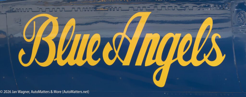 The words “Blue Angels” in yellow script on a dark blue aircraft fuselage.