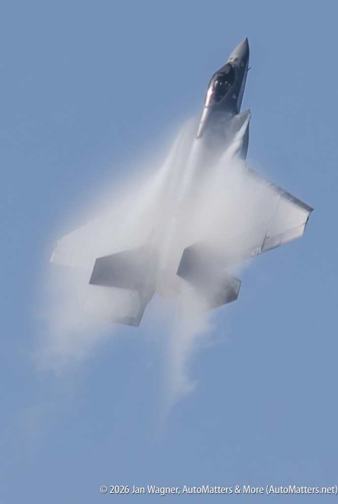 An F-35 fighter jet in flight surrounded by a vapor cloud.