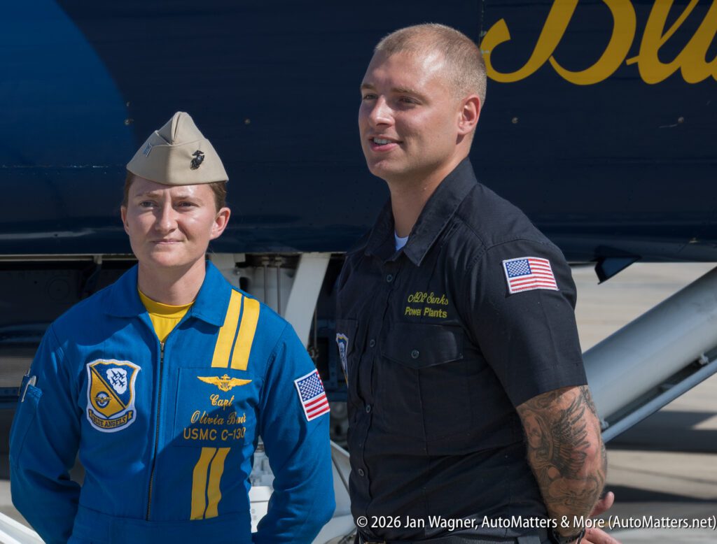 A female U.S. Marine Corps Captain in a blue flight suit and a male Blue Angels maintenance crew member standing in front of an aircraft.