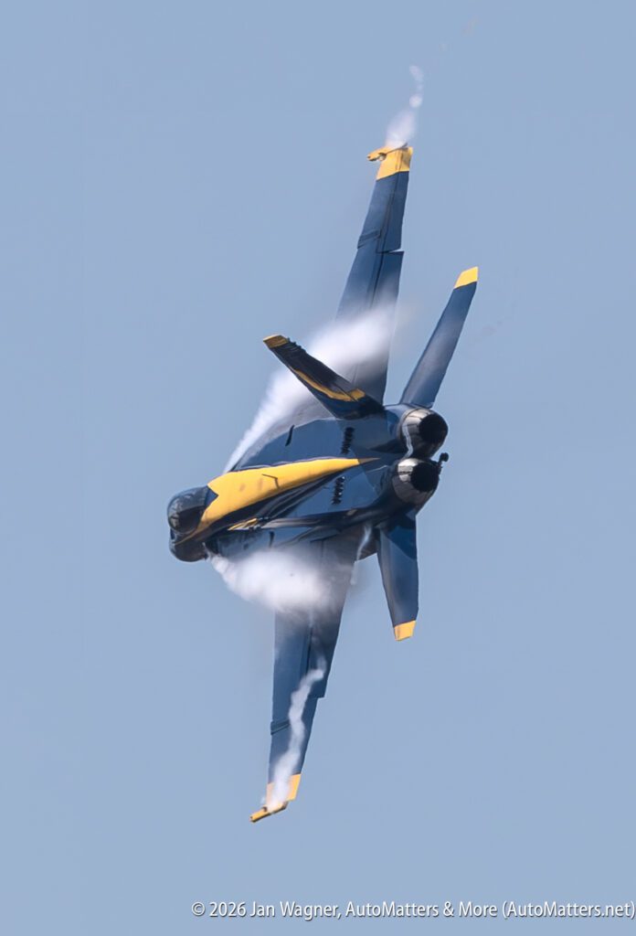 A Blue Angels F/A-18 Hornet jet performing a steep climb with vapor trails.