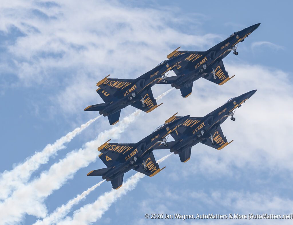 Two Blue Angels fighter jets flying in formation against a blue sky with clouds.