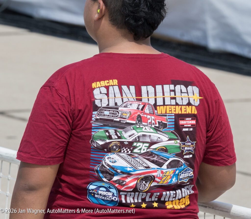 A person wearing a maroon NASCAR San Diego Weekend t-shirt featuring illustrations of three race cars.