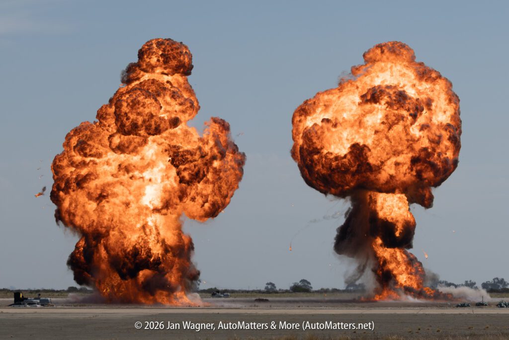 Two large fireballs from explosions rising over a flat airfield.