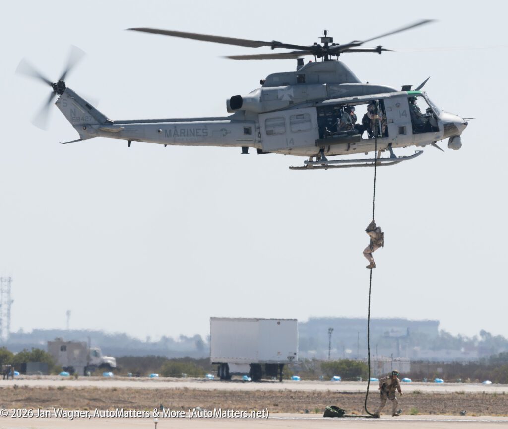 A U.S. Marines helicopter hovering above a runway while a soldier fast-ropes down to the ground.