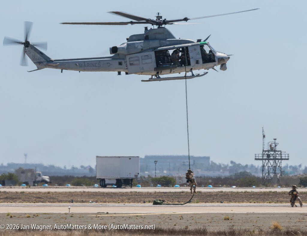 A U.S. Marine Corps helicopter hovering above a runway as a soldier fast-ropes down to the ground.