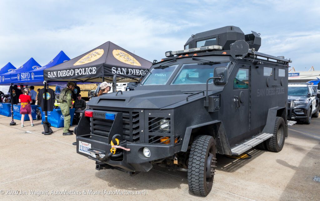 A black San Diego Police Lenco BearCat armored vehicle parked at an outdoor event near a branded tent.
