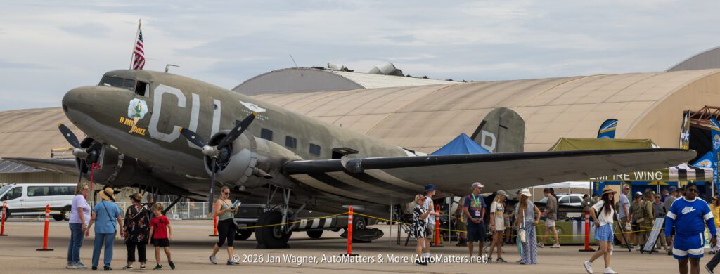 Vintage C-47 transport aircraft named “D-Day Doll” parked on an airfield with spectators nearby.