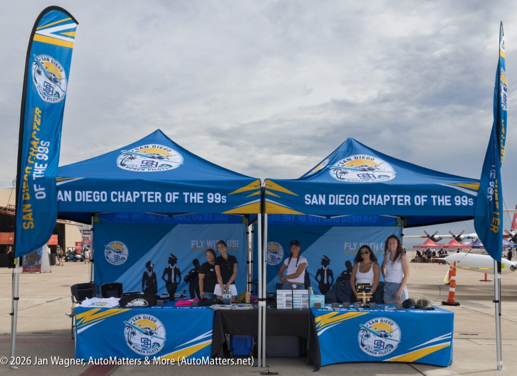 Four women standing at two blue promotional tents for the San Diego Chapter of the 99s at an airfield.