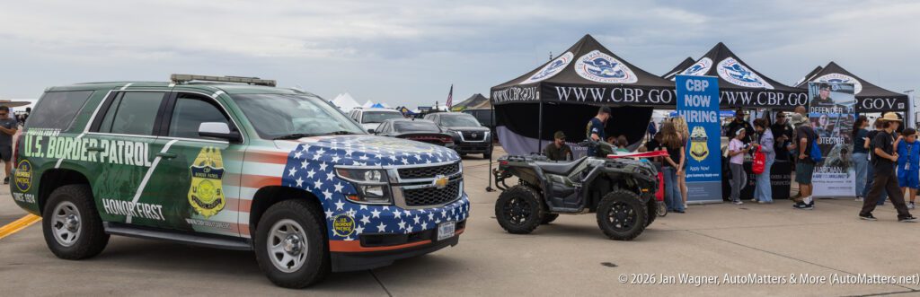 A U.S. Border Patrol vehicle with an American flag livery parked in front of a recruitment tent at an outdoor event.