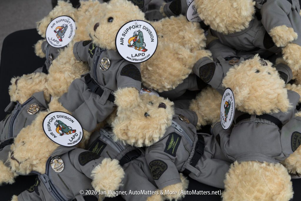 A pile of tan teddy bears wearing grey flight suits with “LAPD Air Support Division” patches and circular stickers.