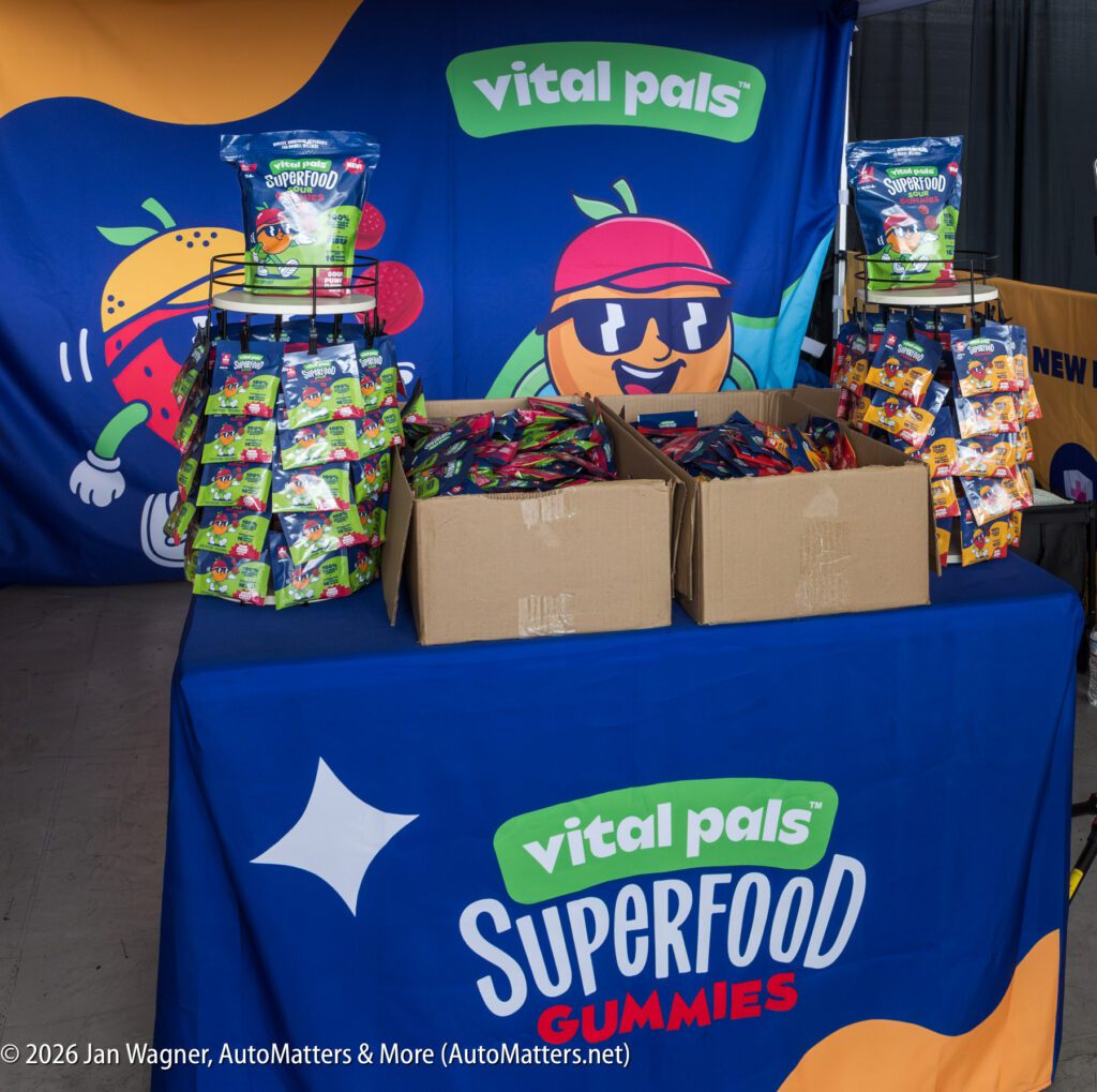 Display table with racks and boxes of Vital Pals superfood gummy pouches in front of a branded blue backdrop.