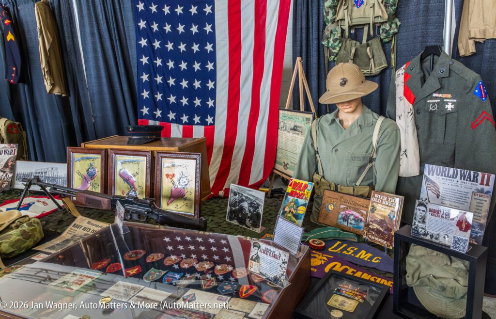 A display of U.S. Marine Corps World War II memorabilia, including uniforms, a pith helmet, medals, historical photographs, and informational signs in front of an American flag.
