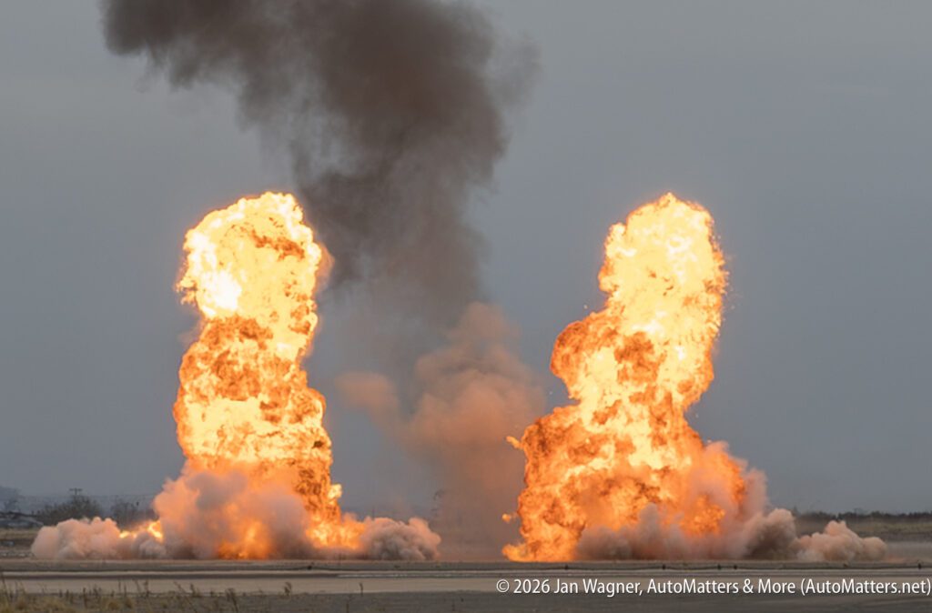 Two large, bright orange fireballs erupt from the ground, sending a thick column of dark smoke into the sky.