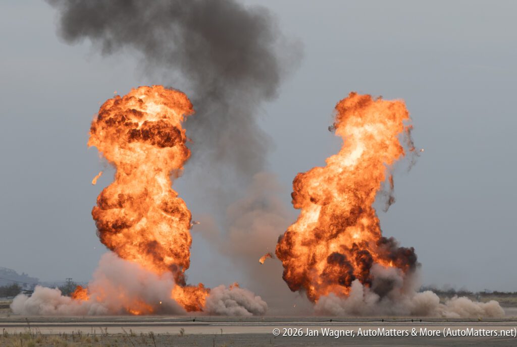 Two large, separate fireballs exploding on a flat, open field.