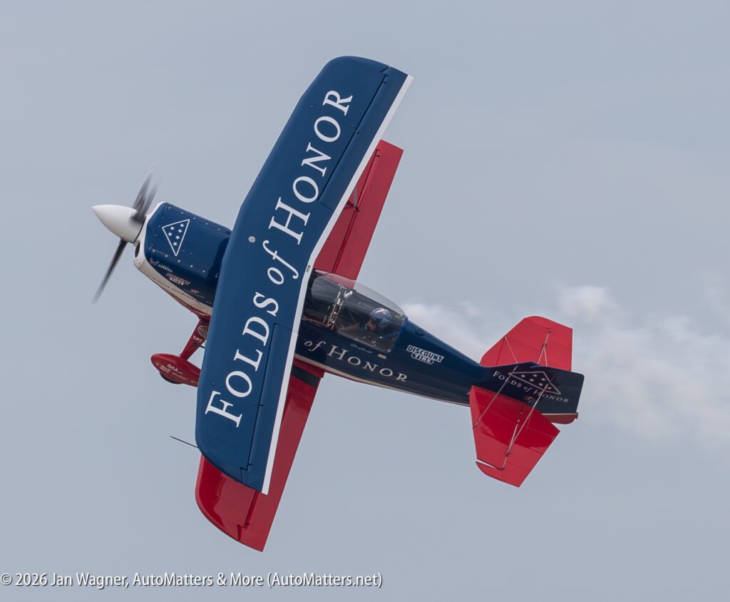 A blue and red aerobatic plane with “Folds of Honor” branding in flight against a gray sky.