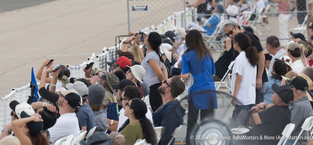 A crowd of spectators sitting in bleachers looking up toward an airfield.