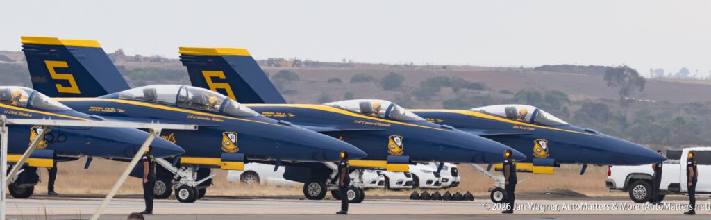 Four Blue Angels F/A-18 Super Hornet fighter jets parked in a line with ground crew standing nearby.