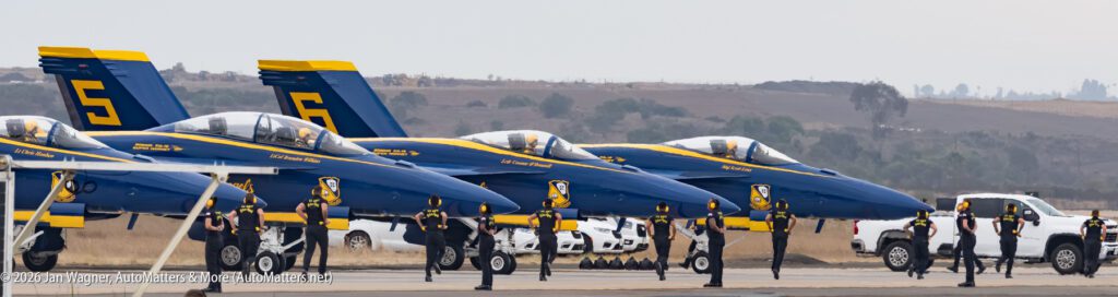 Blue Angels F/A-18 Super Hornet aircraft lined up on a runway with ground crew members standing in front of them.