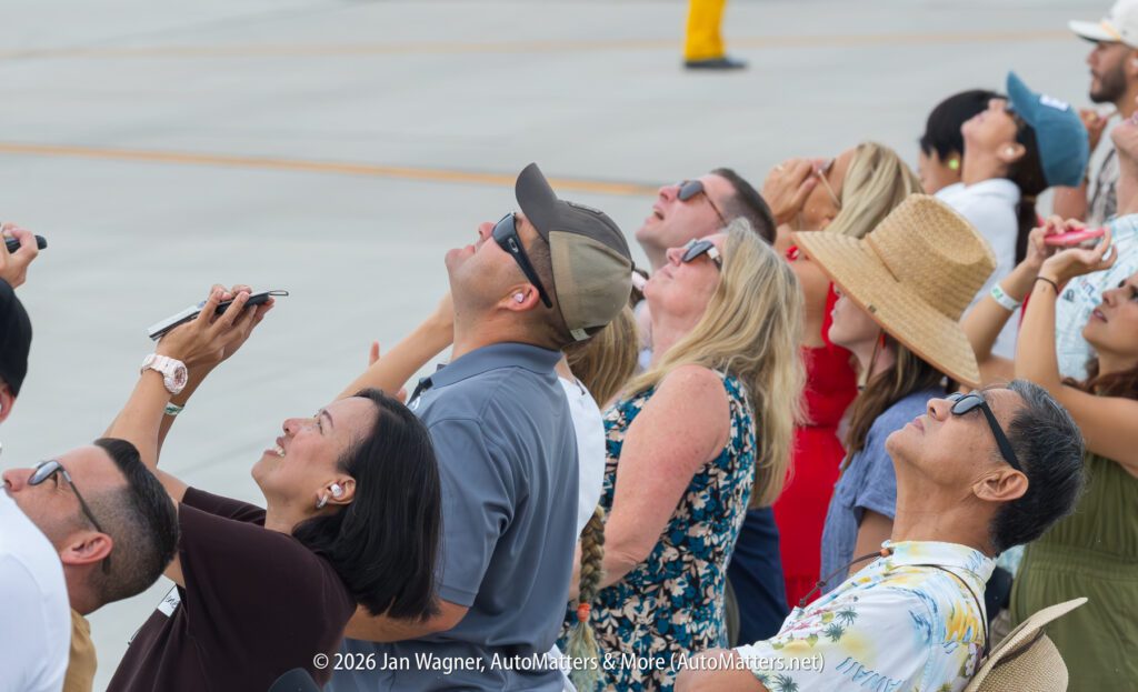 A crowd of people wearing sunglasses and hats looking up at the sky.