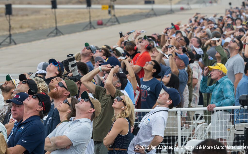 A crowd of people standing behind a fence, looking up toward the sky.