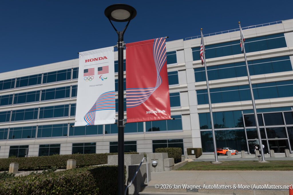 Two Honda banners hanging from a lamp post in front of a multi-story office building.