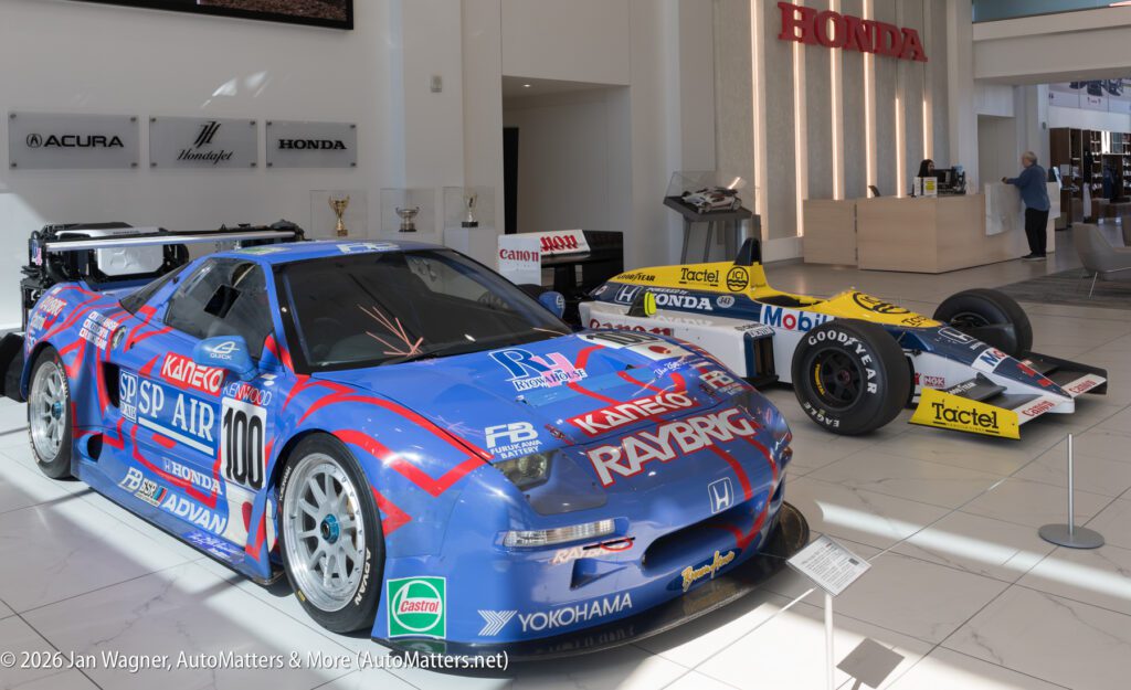A blue Honda NSX race car and a yellow and white formula race car on display in a Honda dealership showroom.
