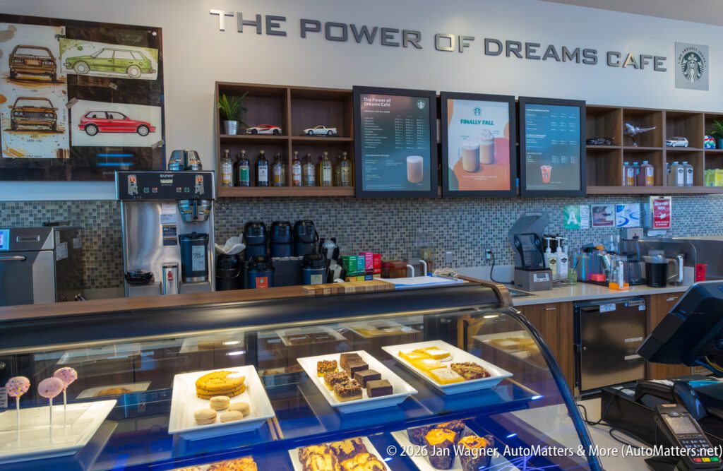 The interior of a Starbucks cafe with a menu board, coffee equipment, and a display case containing various baked goods and cake pops.