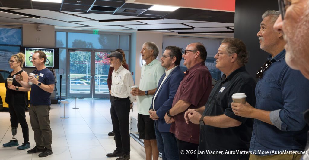 A group of people standing in a line in a car showroom, watching a presentation.