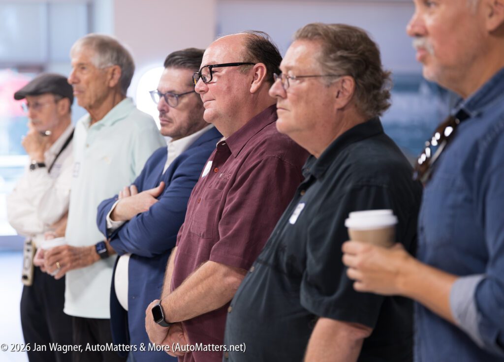 A line of six men standing in profile, looking in the same direction.