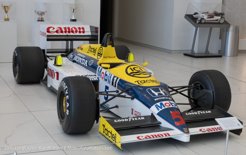 A blue, yellow, and white 1986 Williams-Honda Formula One race car marked with number 5 and sponsor logos on display in a gallery.