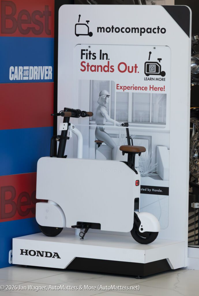 White Honda Motocompacto electric scooter on display with a promotional sign featuring a QR code.