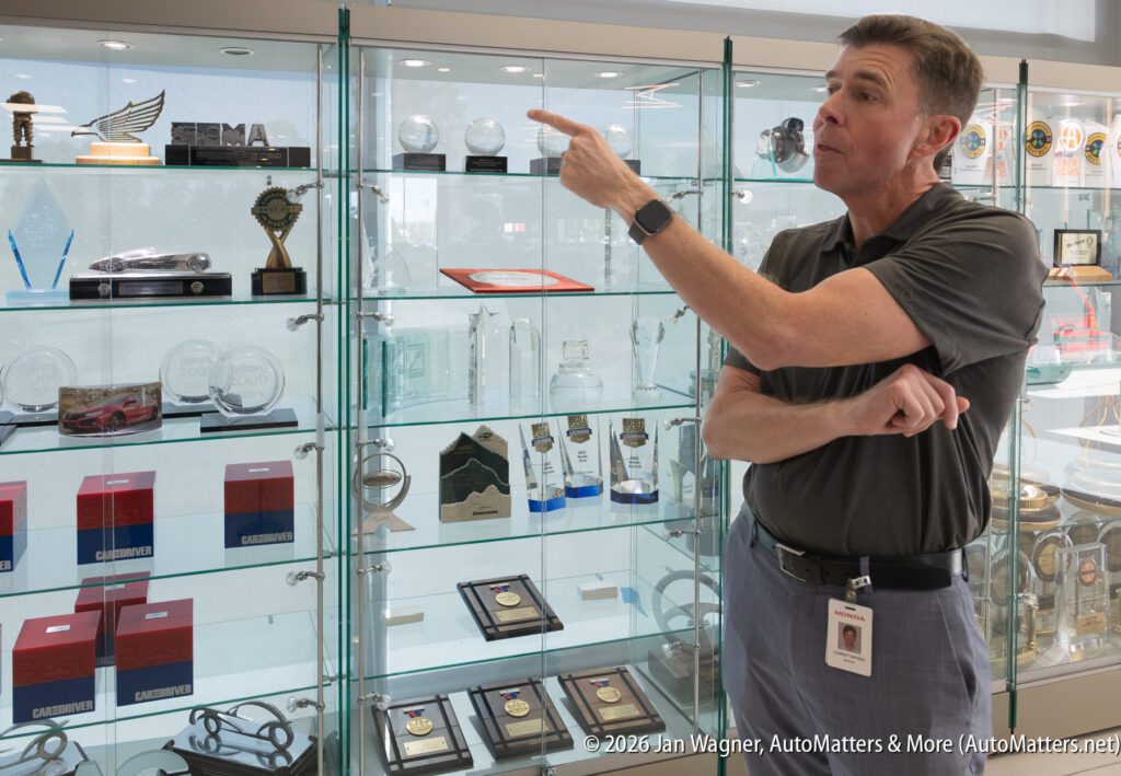 A man in a grey polo shirt pointing toward awards inside a glass display case.