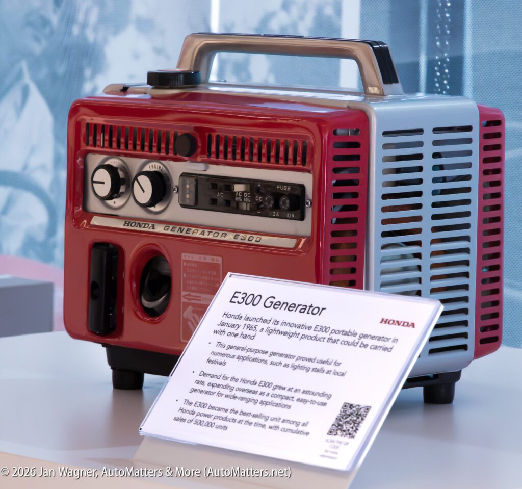 A red and light blue Honda E300 portable generator with an accompanying information placard describing its history and features.