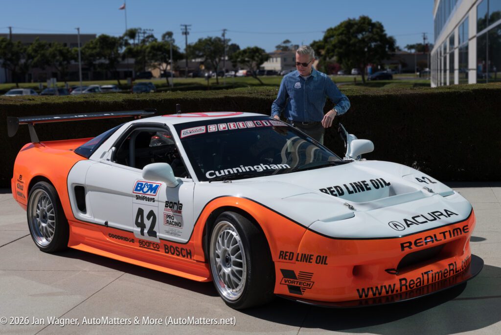 A man stands beside a white and orange Acura NSX race car with the number 42 and various sponsor logos on the body.