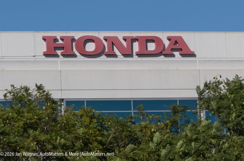 Large red Honda logo mounted on a light-colored building facade above trees.